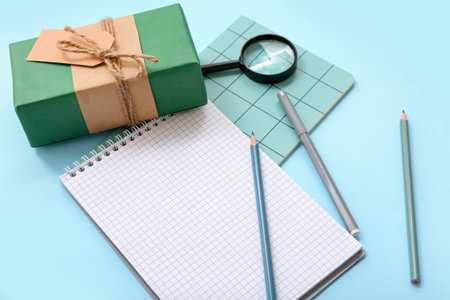 Notebooks with gift box, magnifier and stationery on blue background