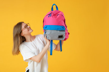 Female student with backpack on yellow background
