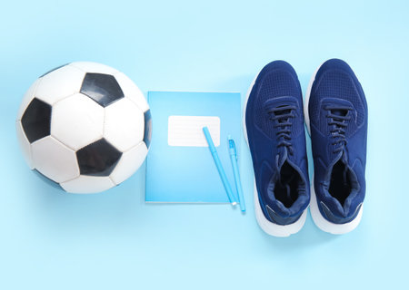 Sneakers with soccer ball, notebook and pens on blue backgroundの写真素材