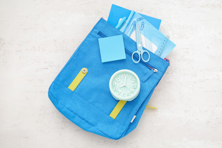 Backpack with alarm clock and different stationery on white background