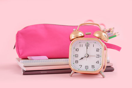 Alarm clock with notebooks and pencil case on pink backgroundの写真素材