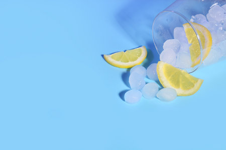 Glass of ice cubes with lemon slices on blue backgroundの写真素材