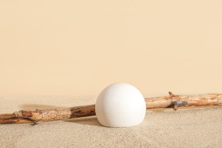 Decorative plaster podium with branch on sand against beige background