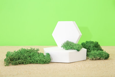 Decorative plaster podium with moss on sand against green background