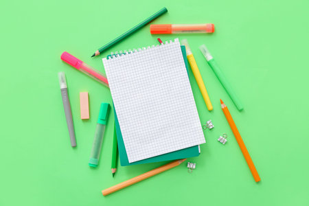 Blank notebook with different stationery on green background