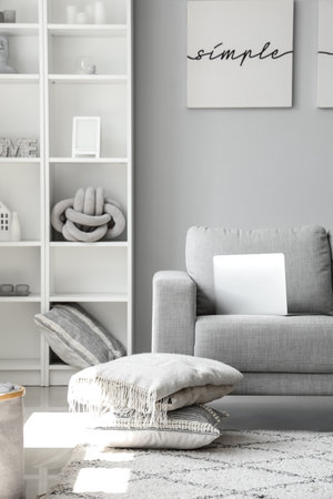 Cozy gray sofa with modern laptop in interior of light living roomの写真素材