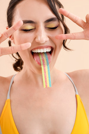 Young woman in swimsuit eating jelly candy on beige background, closeupの写真素材