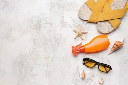 Sunglasses with flip flops, seashells and bottle of sunscreen cream on light grunge background