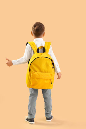Little schoolboy with yellow backpack showing thumb-up gesture on orange background, back viewの写真素材