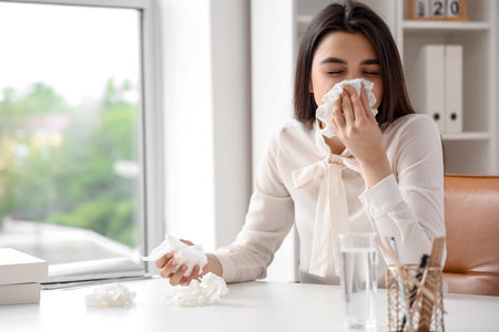 Sick woman with runny nose in officeの写真素材