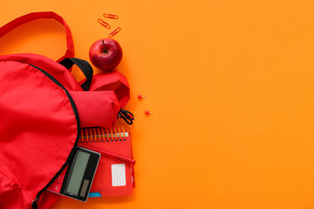 Red school backpack with pencil case, calculator and apple on orange backgroundの写真素材