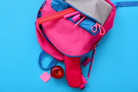 Pink school backpack with apple, ruler and markers on blue backgroundの写真素材