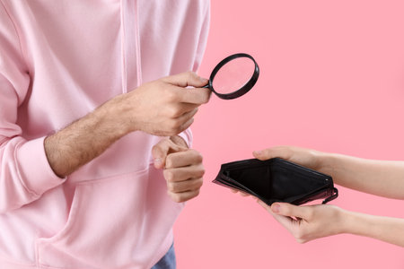Young man with magnifier looking at empty wallet on pink background, closeupの写真素材