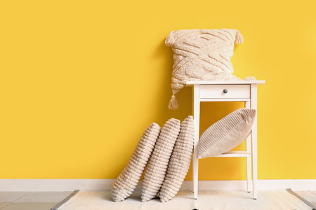 Table with stylish pillows near yellow wall in roomの写真素材