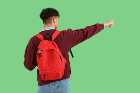 Male student with backpack pointing at something on green background, back viewの写真素材