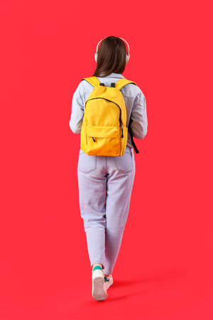 Female student in headphones with backpack on red background, back viewの写真素材