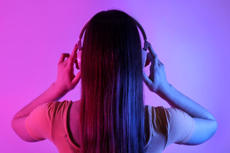 Young woman in headphones listening to music on color backgroundの写真素材