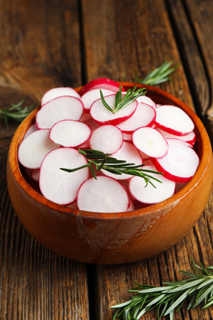 Bowl with slices of fresh radish and rosemary on wooden tableの写真素材