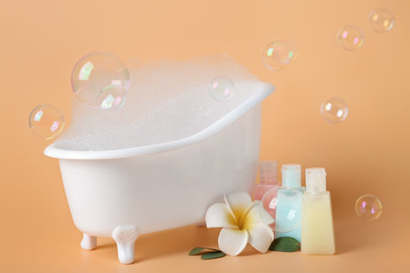 Small bathtub with foam, soap bubbles and bottles of cosmetic products on color backgroundの写真素材
