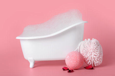 Small bathtub with foam, sponge and bath bomb on pink backgroundの写真素材
