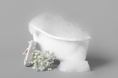 Small bathtub with foam, gypsophila flowers and pumice stone on gray backgroundの写真素材