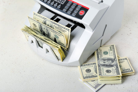 Modern cash counting machine with dollar banknotes on light background, closeupの写真素材