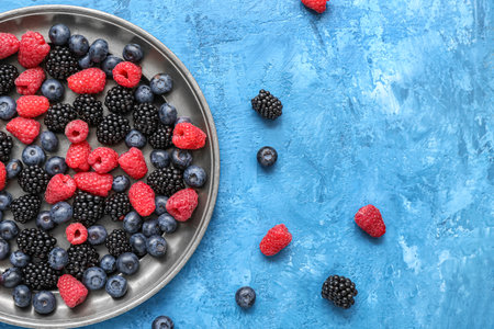 Plate with different fresh berries on blue backgroundの写真素材