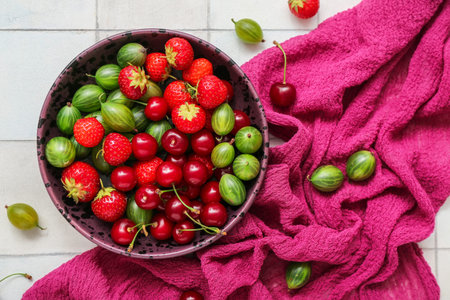 Bowl with different fresh berries on light tile background