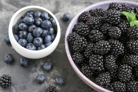 Bowls with fresh blackberry and blueberry on gray background, closeup