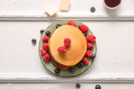 Plate of tasty pancakes with raspberries and blueberries on white wooden background