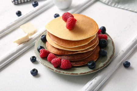 Plate of tasty pancakes with raspberries and blueberries on white wooden background