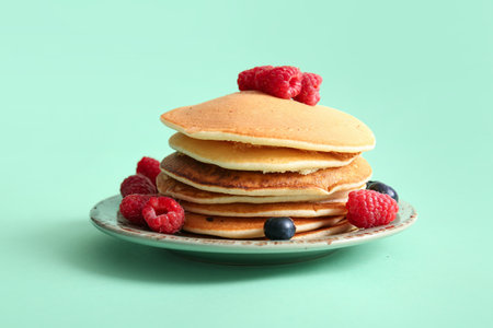Plate of tasty pancakes with raspberries and blueberries on turquoise backgroundの写真素材
