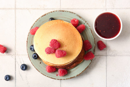 Plate of tasty pancakes with raspberries and blueberries on white tile background