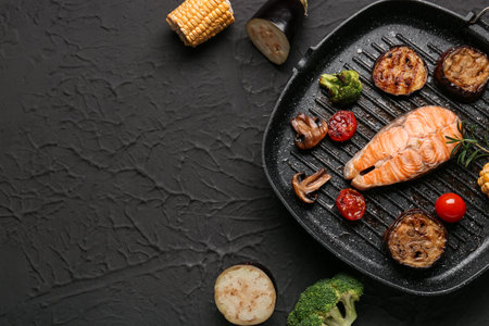 Frying pan with tasty grilled salmon steak and vegetables on black backgroundの写真素材