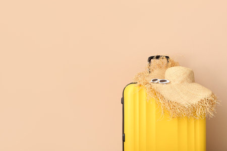 Suitcase with wicker hat and sunglasses near pale orange wall. travel conceptの写真素材