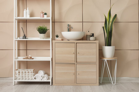 Interior of bathroom with sink bowl, wooden cabinet and shelving unit near beige wallの写真素材