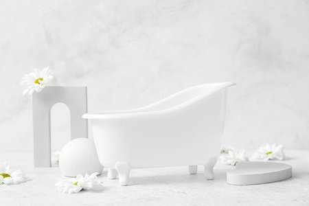 Small bathtub, chamomile flowers and decor on light background