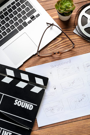 Storyboard with movie clapper, laptop and eyeglasses on wooden background