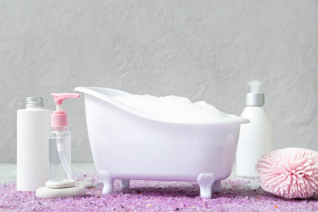 Small bathtub with foam, cosmetic products, sponge and sea salt on grunge backgroundの写真素材
