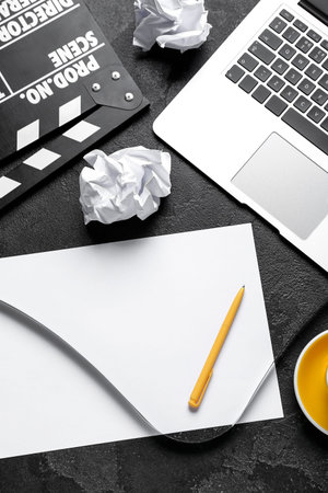 Blank paper sheet with movie clapper and laptop on dark backgroundの写真素材