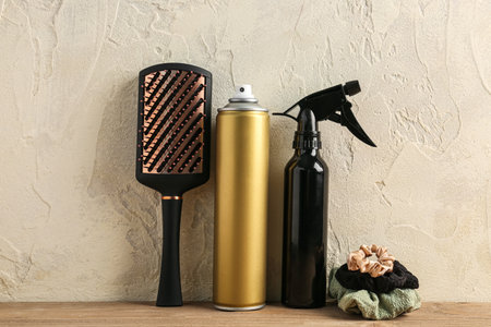 Different bottles of hair sprays, brush and scrunchy on table near light wallの写真素材