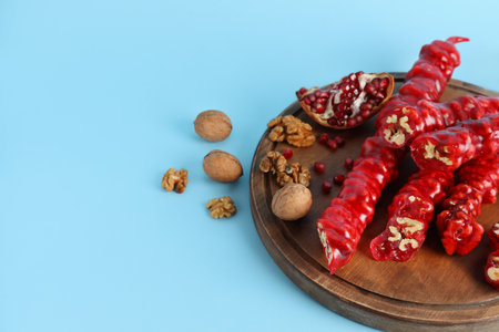Wooden board with tasty churchkhela, walnuts and pomegranate on color backgroundの写真素材