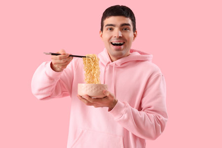 Surprised young man with bowl of Chinese noodles on pink backgroundの写真素材