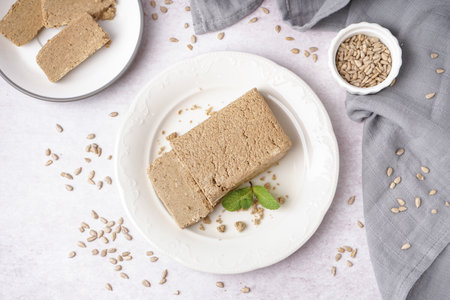 Plate with tasty halva and sunflower seeds on white backgroundの写真素材