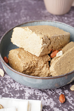 Bowl with pieces of tasty halva and peanuts on gray background
