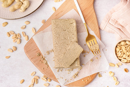 Board with tasty halva and peanuts on white background