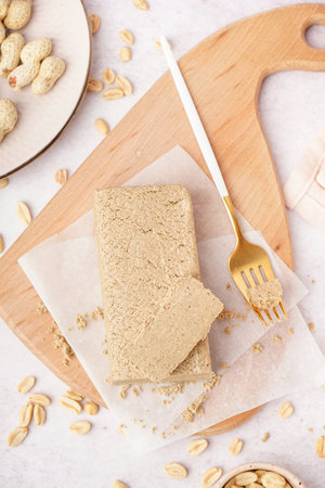 Board with tasty halva and peanuts on white background