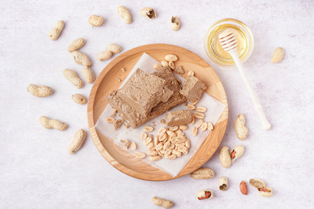 Wooden plate with pieces of tasty halva and peanuts on white backgroundの写真素材