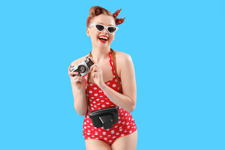 Young pin-up woman in swimsuit with photo camera on blue backgroundの写真素材