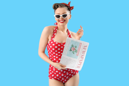 Young pin-up woman in swimsuit with newspaper on blue background